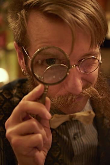 Ein Mann im Steampunkstil schaut uns durch eine Lupe an