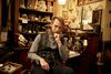 Ein Mann in Steampunk- Optik sitzt in seinem warm und heimelig erleuchteten Museumsraum. Hinter ihm steht ein Tisch mit gläsernen Gefäßen und es hängen Dinge aus vergangenen Zeiten an den Wänden.