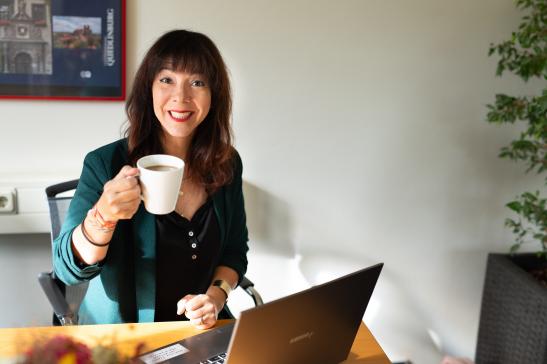 Social Media - Claudia Wolf, grüßt freunlich mit einer Kaffeetasse
