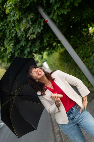 Frau in fragender Pose gen Himmel mit offenem Regenschirm in der Hand