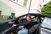 Eine Frau öffnet die Tür ihres Wagens innen sitzend und lächelt in die Kamera.