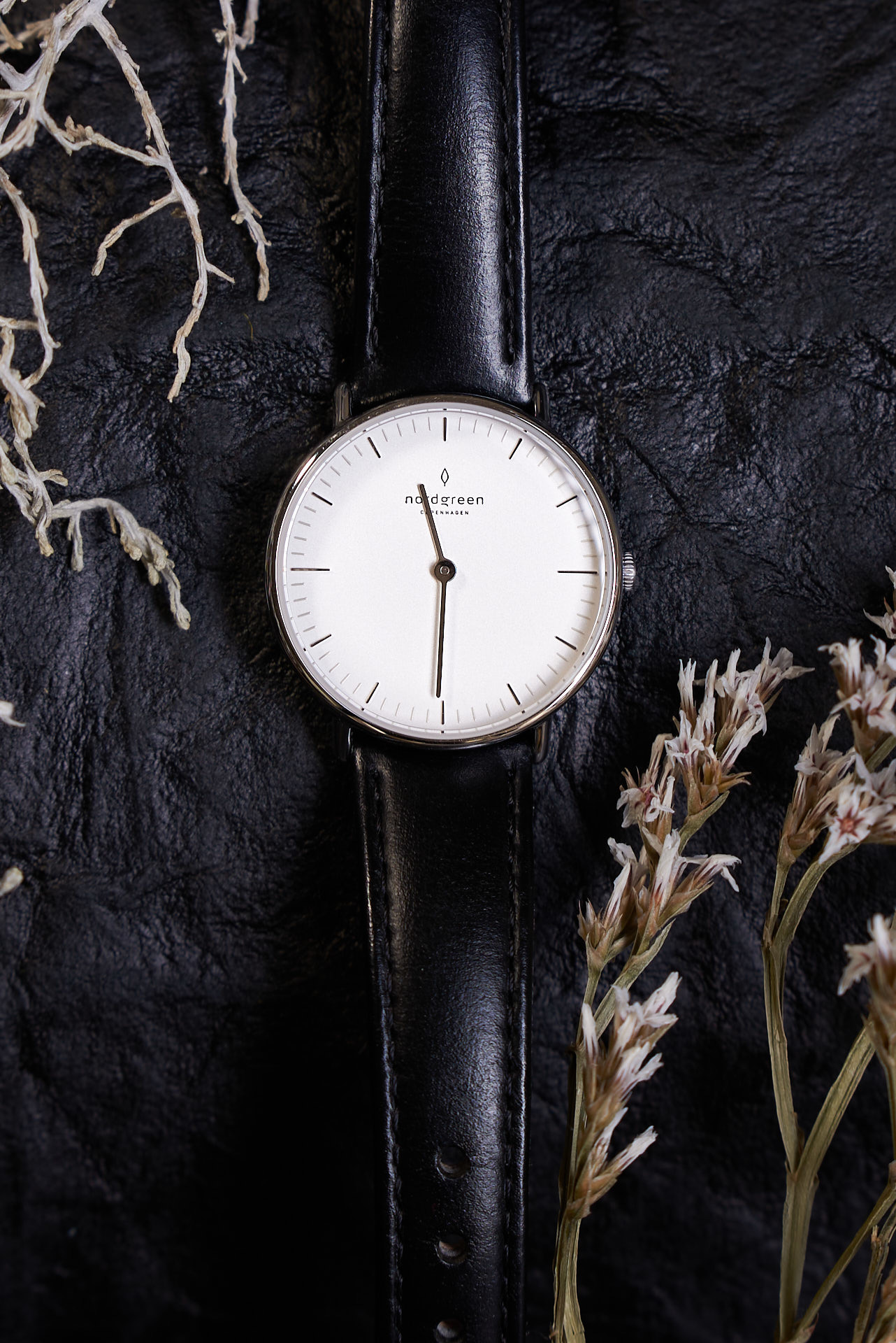 analoge Uhr auf schwazen Untergund umspielt von dezentem Geäst
