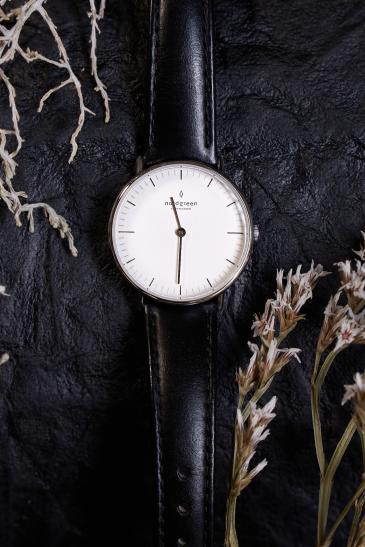 analoge Uhr auf schwazen Untergund umspielt von dezentem Geäst